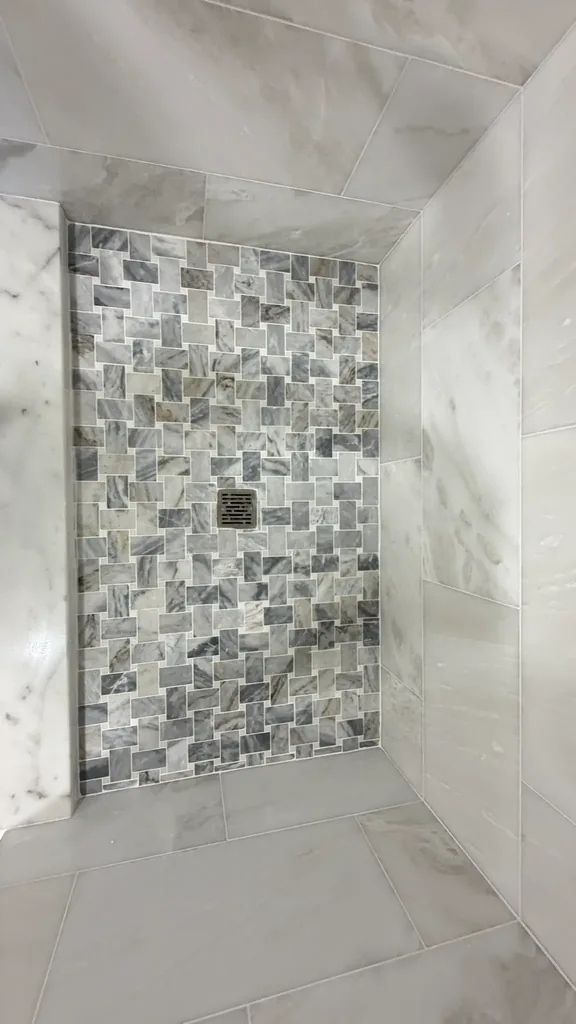 Close view of gray and white shower floor mosaic around a square drain, photographed at a sideways angle
